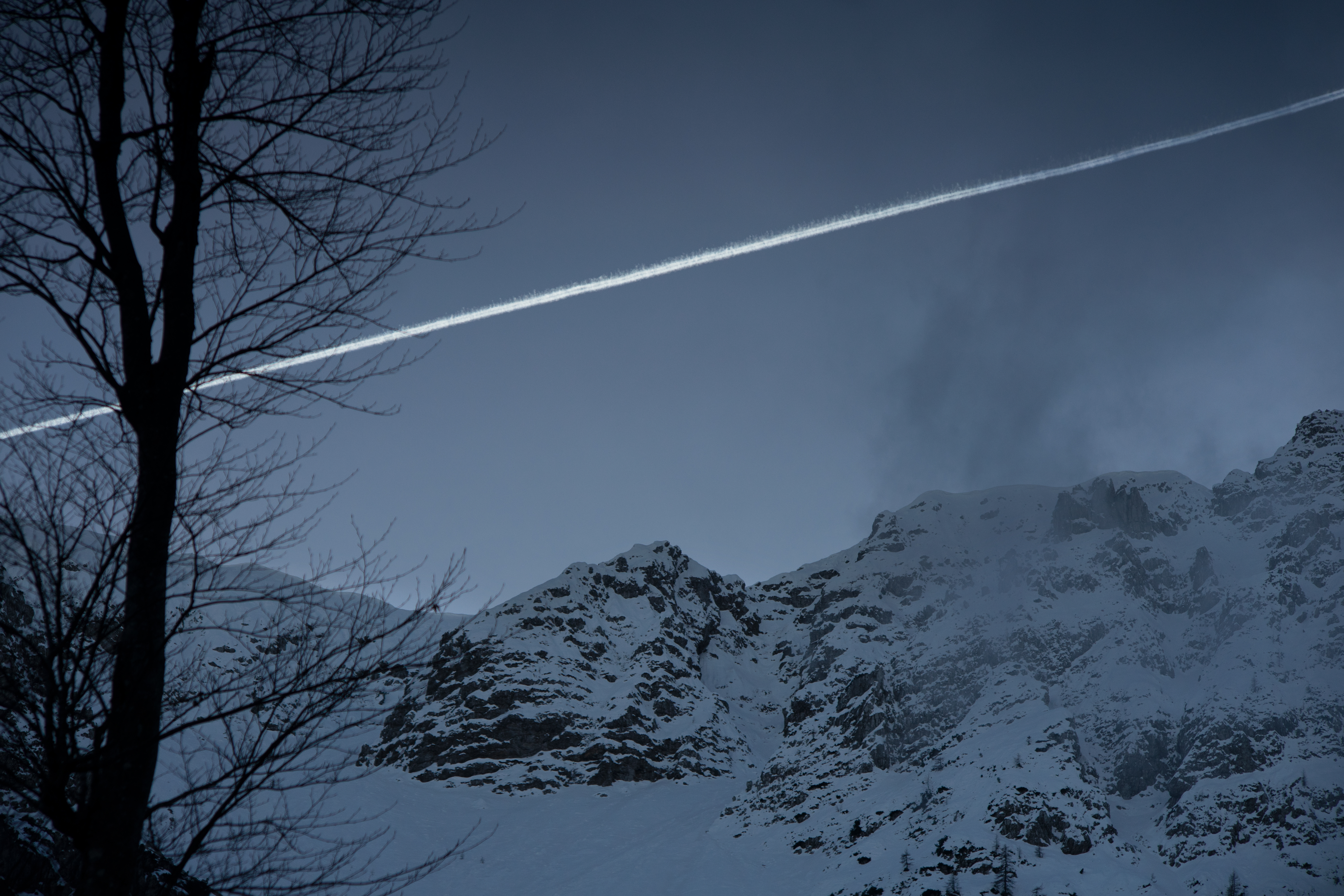 A dark blue image of mountains and a frozen chem trail in the sky. Creative Commons